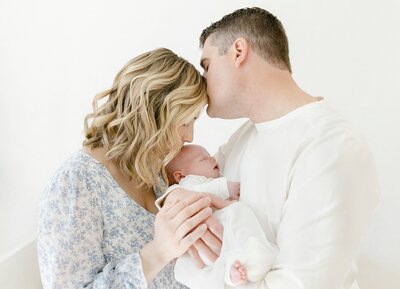 Dad kissing mom on forhead as they hold newborn baby in charlotte newborn portrait photography session.