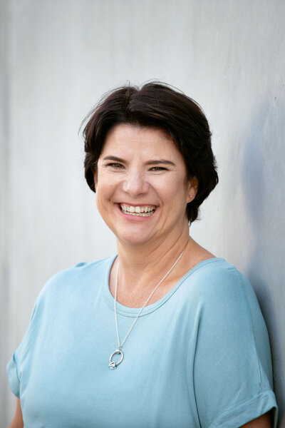 Portrait of photographer Bronwyn Mostert standing against plain wall outdoors