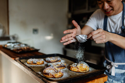 A baker sprinkling powdered sugar on his sweet breads.