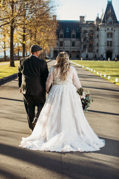 Photo of bride and groom walking towards the historic Biltmore showing off back of bride's dress