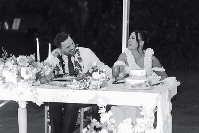 A wedding couple sitting together at their reception laughing 