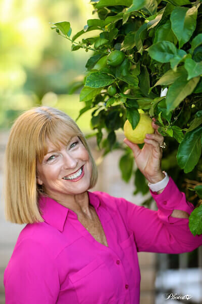 Lora Ulrich in a grey sleeveless top holding a mug, smiling at the camera.