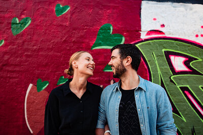 Couple standing looking at each other lovingly. Standing in front of a graffiti wall.