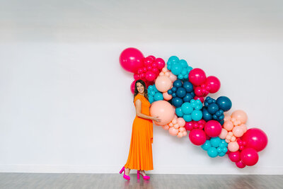 The expertise of Air with Flair, your go-to for premium balloons, decor, and rentals. The expert, dressed in a pink t-shirt and black pants, is crafting a stunning pink and blue balloon installation for the next unforgettable celebration.