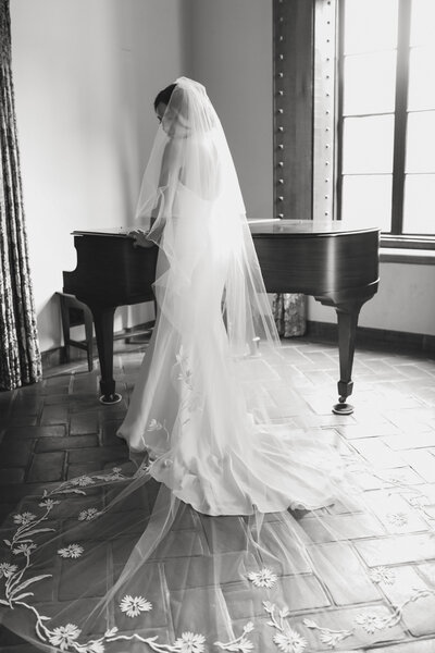 bride wearing her wedding dress while she stands next to a grand piano