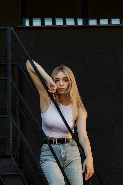 A woman leaning against a metal stair rail. Representing someone who has benefited from body image therapy in Manhattan. She was able to start her journey to self-love with support from a body image therapist.