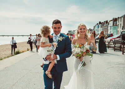 Bride and groom walking across Deal beach with their daughter on their wedding day