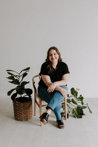 Therapist sits in chair with legs crossed while smiling surrounded by plants