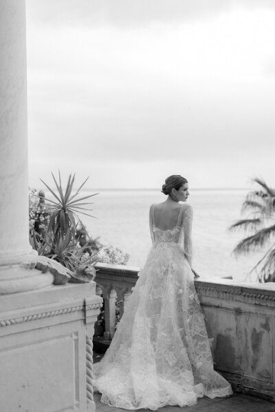 Bride and groom smiling on stone steps outside a building, bride with a trailing veil.