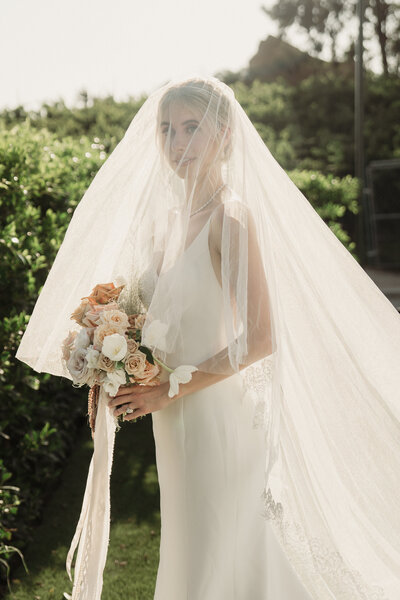 bride in long veil with blusher holding an ethereal bouquet with ribbons hanging about to walk down the aisle at hummingbird  nest ranch captured by los angeles wedding photography team magnolia west