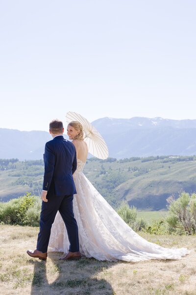 Bride and groom walking with the bride holding a white paper umbrella