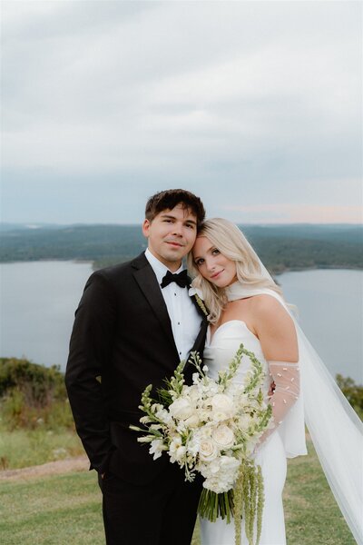 Timeless wedding photo of bride and groom at their wedding standing in front of an overlook with Greers Ferry Lake in Arkansas in the back