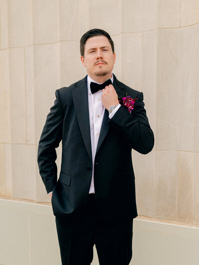 A groom adjusts his bow tie in a formal portrait.