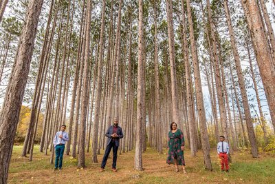 a family of four poses in front of tall trees