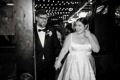 Black and white image of bride and groom holding hands and walking
