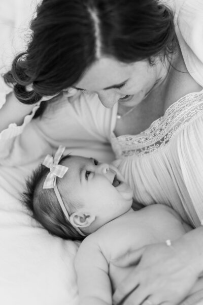 A northern virginia newborn photography photo of a baby girl smiling up at her mother on a white bed