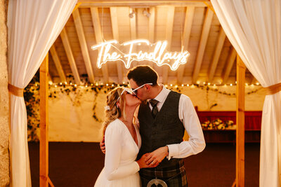 Bride and groom kiss under neon sign at alternative scottish wedding