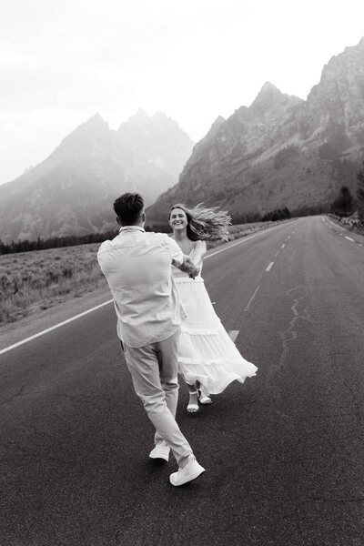 Man and woman dancing in the middle of a road with mountains in the distance