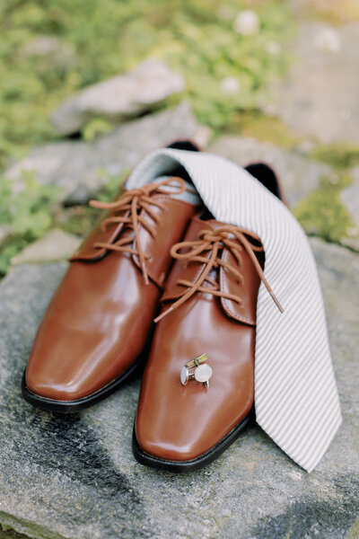 A tie and jewelry sitting on top of dress shoes 
