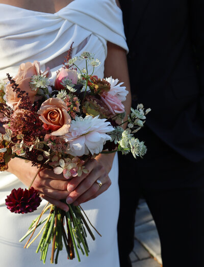 Wedding couple holding lush romantic bouquet with blush roses, burgundy dahlias and eucalyptus at Ottawa micro wedding venue, highlighting elevated floral design for intimate celebrations