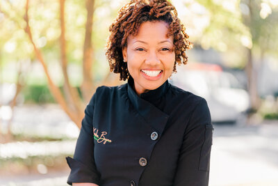 Headshot of female chef in black chef's coat smiling at the camera