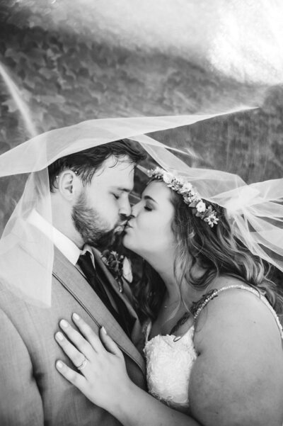 black and white photo of couple kissing under brides veil