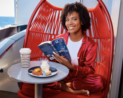 Virgin Voyages balcony deck with a woman sitting in a red chair reading a book