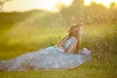 Girl in ball gown smelling flowers in field