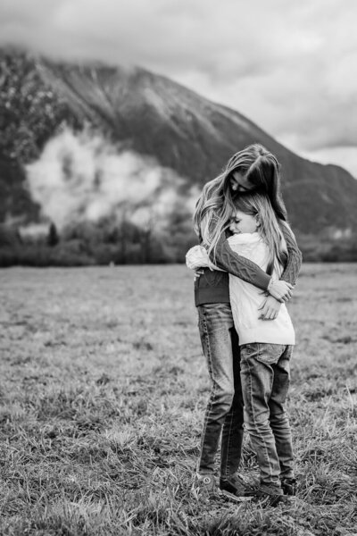 Sisters hugging against a mountain backdrop during a family photoshoot session in Snoqualmie, WA