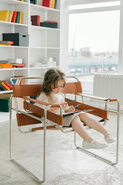 Little girl sitting in a leather and metal chair while coloring in a coloring book