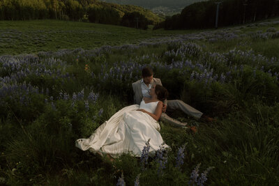 Bride and groom laying in mountain meadow surrounded by Lupine