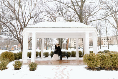 Couple kissing in a gazebo surrounded by snow.