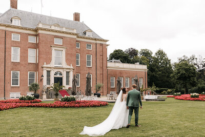 Bruid en bruidegom lopen hand in hand door de tuin van Slot Zeist, de bruidsjurk met sleep, perfect georganiseerd door een weddingplanner en ceremoniemeester