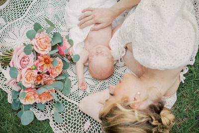 Blonde mother lays on crotchet blanket with her newborn baby next to roses during her Northern VA photo session.