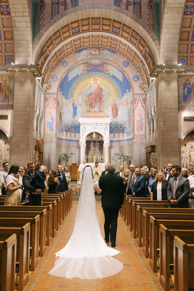 bride and father walking down the aisle at wedding ceremony in a grand church 