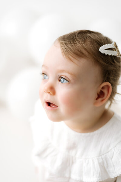 Little girl looking up with white balloons behind her at Billingshurst  cake smash photoshoot