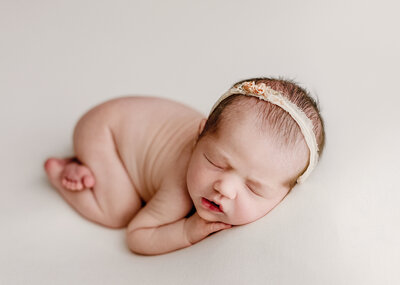 newborn photographer near me poses baby girl in denver studio on an all white blanket with pretty flowers