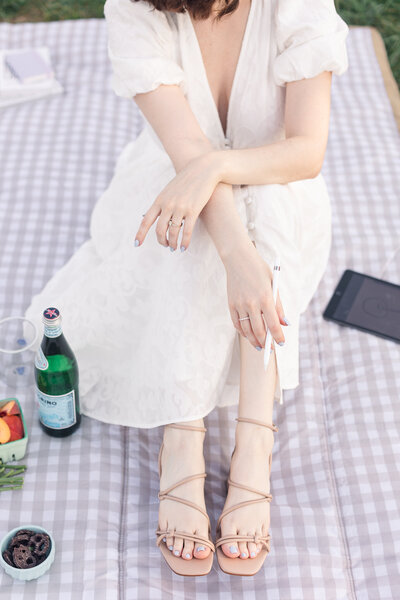 a woman seated on a picnic blanket holds her apple pencil casually in her hand