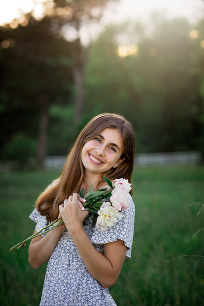 Gorgeous sun-filled senior picture of a pretty girl walking in a field in a floral red dress