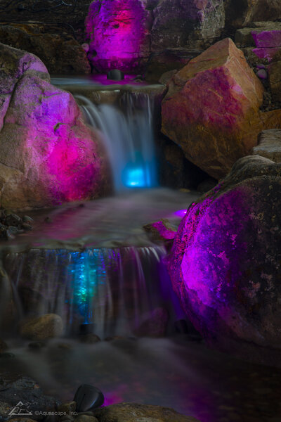 Vibrant purple, blue, and magenta lights reflecting off water in waterfall