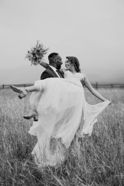 black and white image groom carrying bride in field