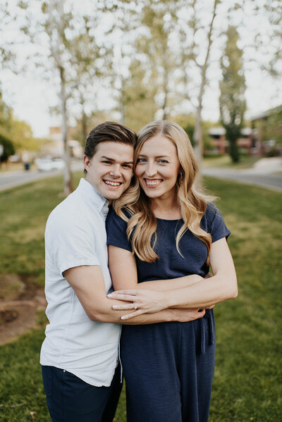 Guy holding his fiance from behind while they smile at the camera during their engagement session