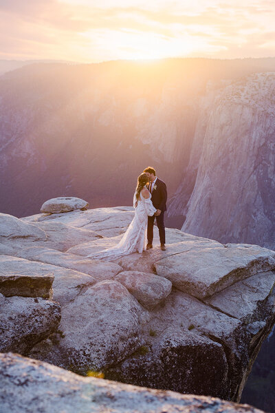 A bride and groom stand on the back of their truck while hugging on their winter mountain wedding day. 