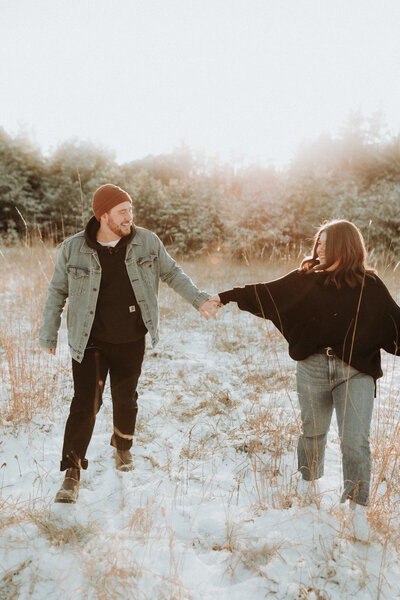 A man and a woman holding hands facing each other in a snowy field at sunset.