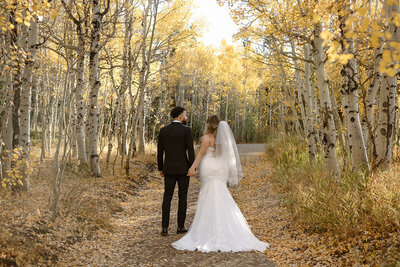 bride and groom walk through a tunnel of golden aspen trees in the rocky mountains.