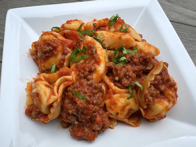 Smartphone displaying the Supper Club meal planning app with weekly menus, next to fresh produce spilling from a grocery bag.