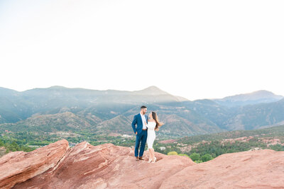 Engaged couple standing on a red rock overlook at sunset during their engagement session.