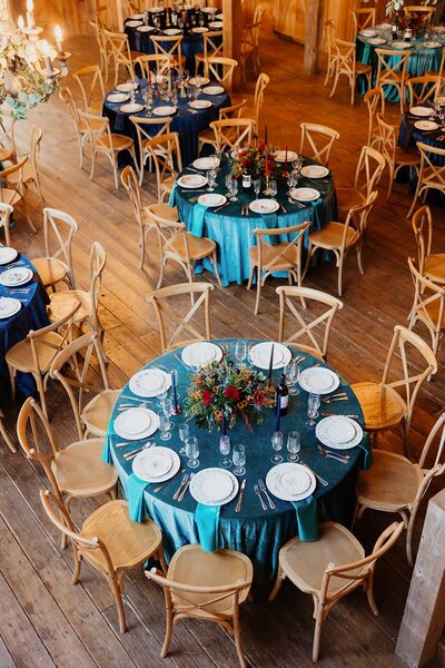 Top down view of tables at wedding reception with teal table cloths and wood chairs