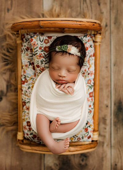 Portrait of newborn girl wrapped and laying on a floarl printed mattress in a little bed