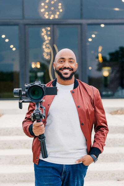 The Award Winning Dallas Fort Worth videographer and photographer Mente Bezuneh from Mentopia Weddings smiling while holding a cinematic camera